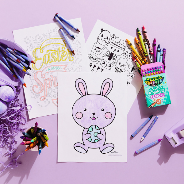 Three Easter coloring pages on a light purple surface, surrounded by crayons.