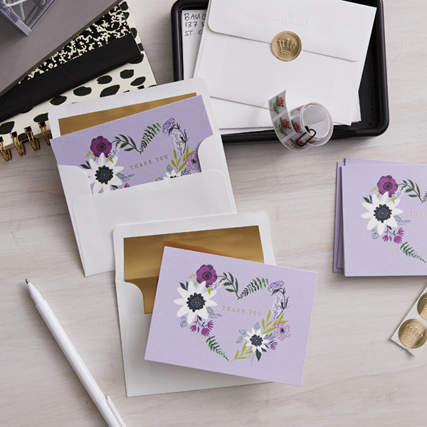 A set of thank you notes with lilac colored covers lie on a light wood surface.
