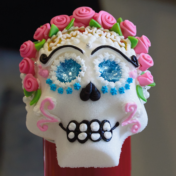 Sugar skull decorated with pink icing roses, blue foil eyes, and other colorful embellishments.