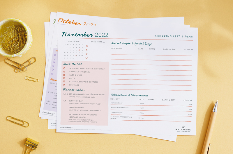 A printable celebration planner page for November sitting on a yellow desk surface with a paperclip cup and pen nearby.
