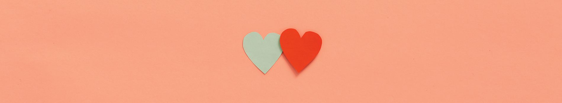 A mint-colored heart and a red heart on a peach colored background