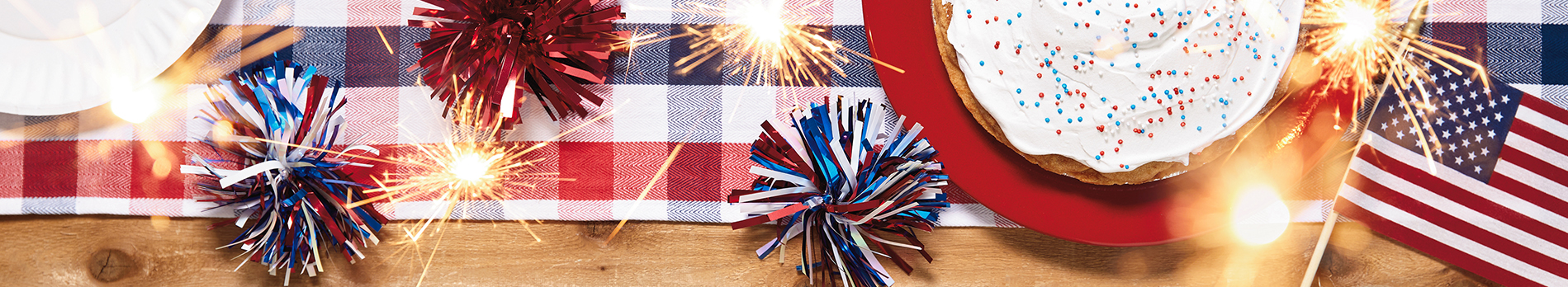 Fourth of July background with sparklers, cake with red, white and blue sprinkles, and checkered table runner