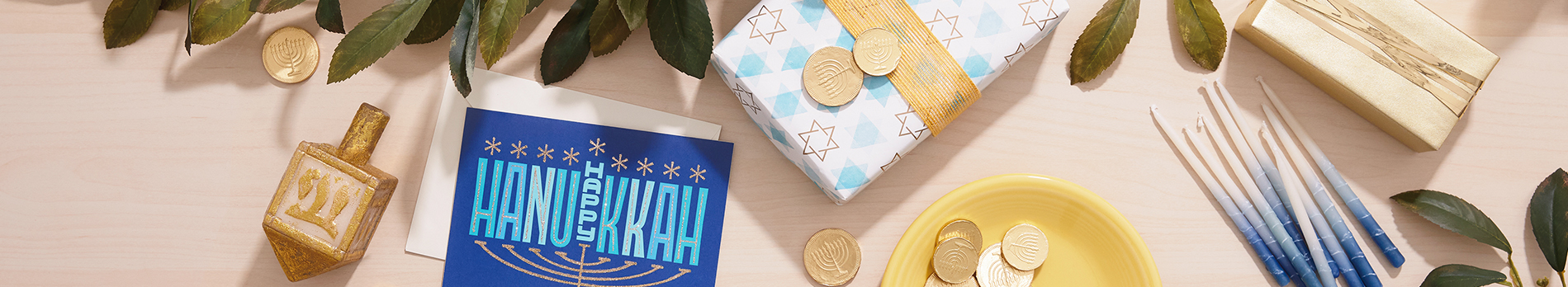 Hanukkah background with dreidel, wrapped gifts, blue candles and gold coins on a tabletop.