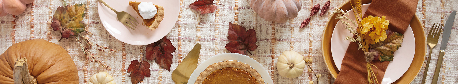Thanksgiving background with place settings, pumpkin pie and fall boards scattered on a rustic linen tablecloth.