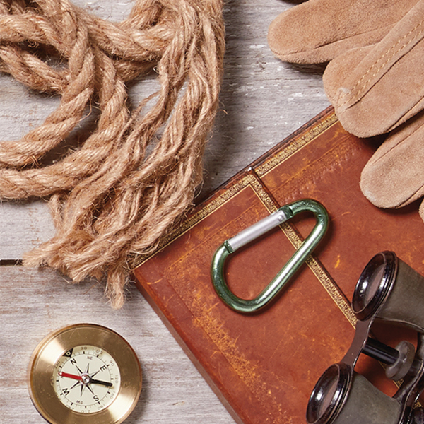A journal, compass, binoculars, rope and leather gloves laid on a wooden tabletop.