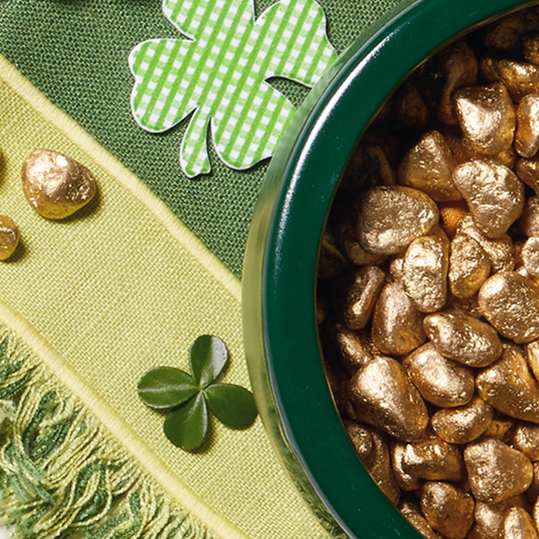 A green bowl filled with pebbles painted gold on a green table runner that's scattered with green and white checkered shamrocks.