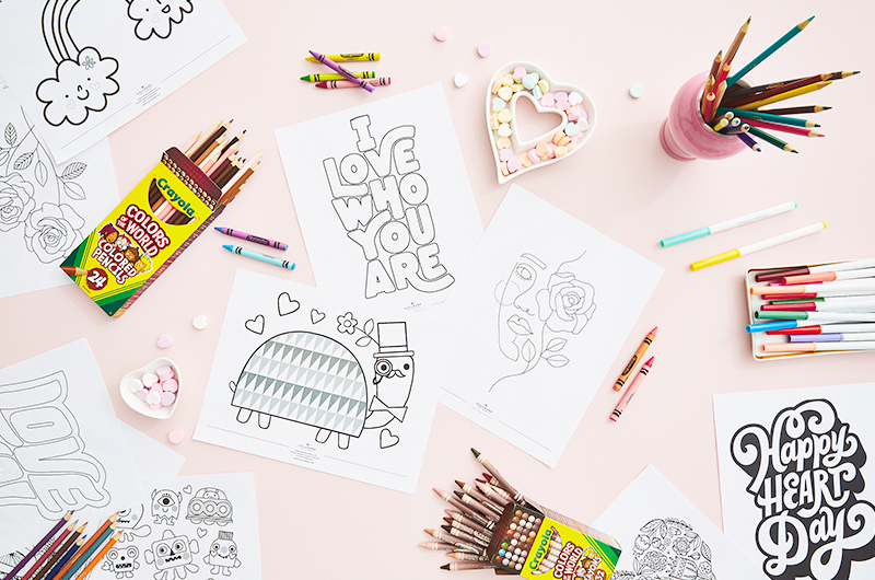 A downshot of various free printable Valetine's Day coloring pages on a table top scattered with Crayola crayons, colored pencils and markers.