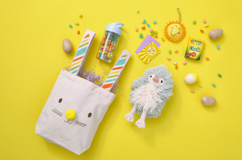 A kids' outdoor-themed Easter care package with a Little World Changers water bottle, Crayola sidewalk chalk, a plush baby chick, and a canvas tote with a bunny face on it.