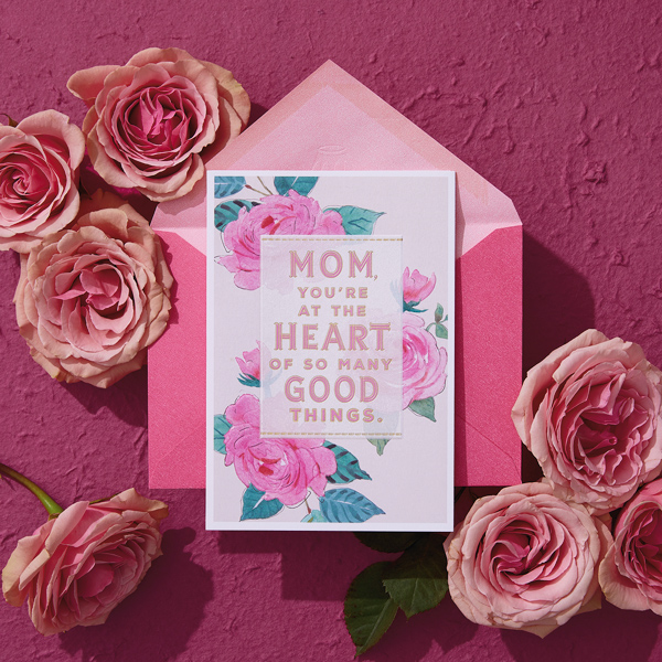 A birthday card for Mom, laying on top of a bright pink envelope and surrounded by pink roses.