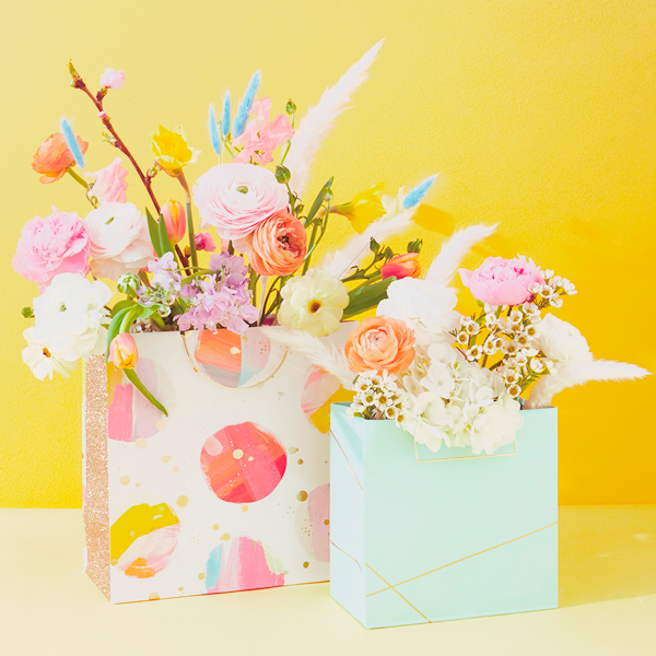 Two brightly colored gift bags filled with spring flower arrangements.