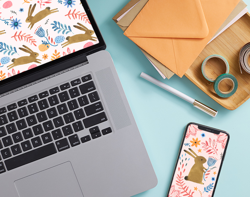 A laptop and smartphone showing spring-themed digital wallpapers that feature brown bunnies.