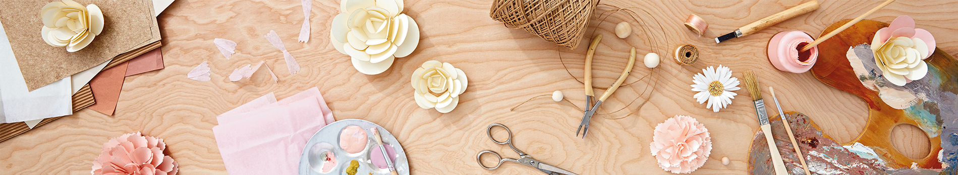 Arts and crafts supplies like paper flowers, twine, paint and scissors scattered on a wood grain tabletop.