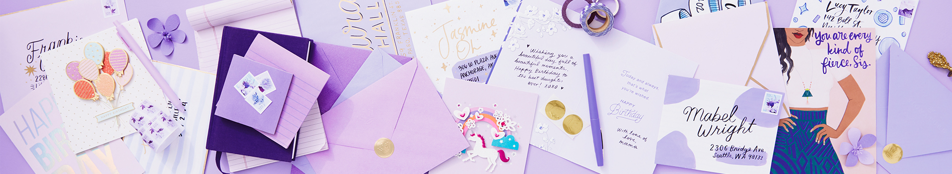 A variety of greeting cards and addressed envelopes in different hues of purple scattered on a tabletop.
