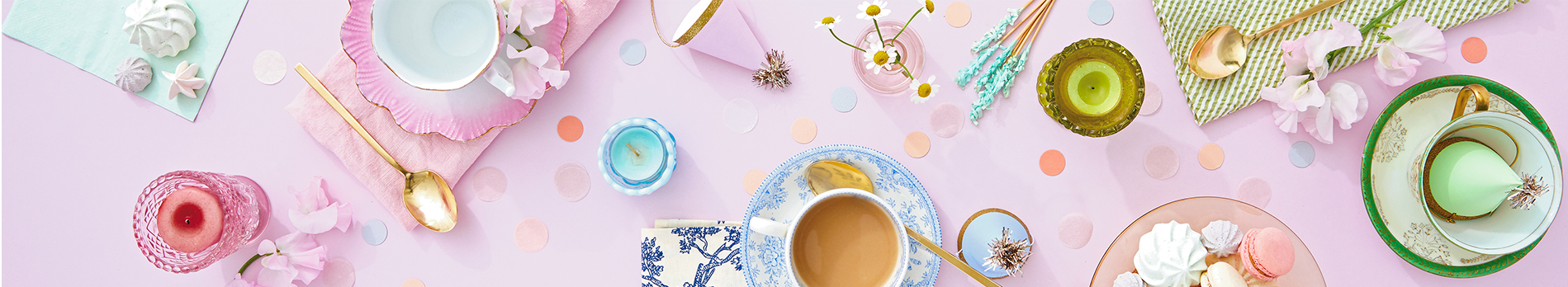 A tea party laid out on a pink tablecloth with colorful polka dot confetti strewn around.
