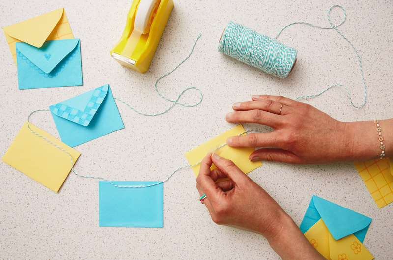 Hands using tape to stick the back of a mini envelope to a piece of twine.