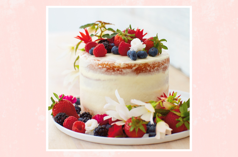 A cake with white icing topped with a variety of summer berries and white flowers.