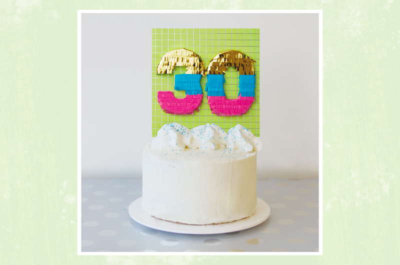 A milestone cake topper made from a 30th birthday card, sitting on top of a white cake with blue sprinkles.