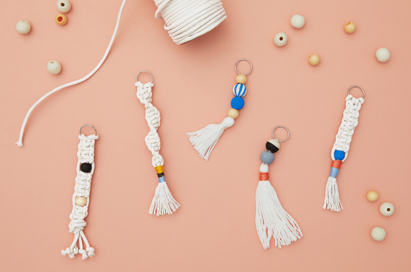 A variety of DIY macramé keychains laid out on a peach-colored surface, surrounded by wooden beads.