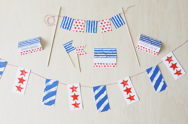 A cake topper, banner and food labels that feature blue and white stripes and red stars.