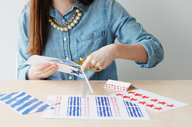 A woman cutting out flags from the free printable page.