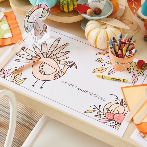 A Thanksgiving kids table setting featuring a coloring placemat and a DIY place card.