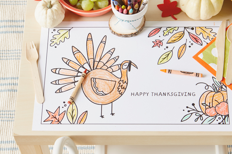 A kids Thanksgiving coloring placemat featuring a turkey and fall leaves.