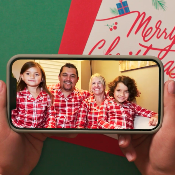 Hands holding a smartphone showing a video of a family clad in matching red, flannel holiday pajamas.