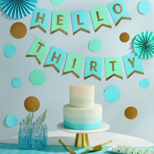 A thirtieth birthday party table with a white and turquoise cake, surrounded by Color Pop party decorations in colors of light blue, turquoise and gold.