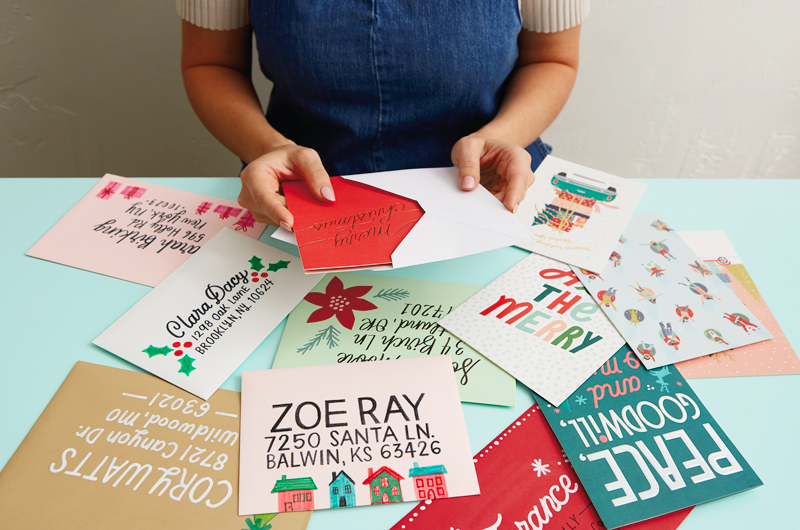 A woman sits at a table covered in Christmas cards and brightly decorated envelopes.