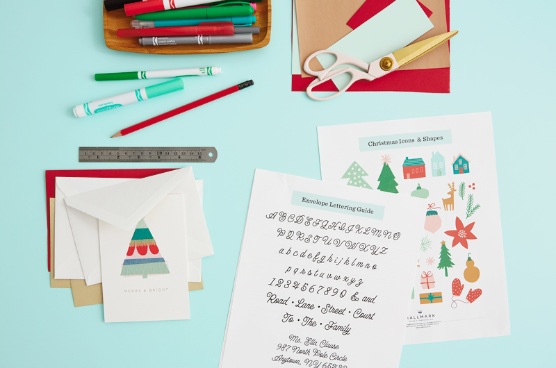 Materials needed for lettering Christmas envelopes include holiday cards and envelopes, a ruler, a pencil and markers, scissors and construction paper, and our free printable Christmas envelope lettering guide.