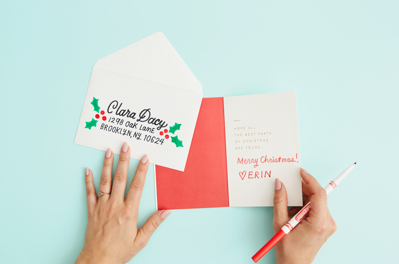 A hand lettered envelope and a woman's hands holding an open Christmas card; the inside message reads, 
