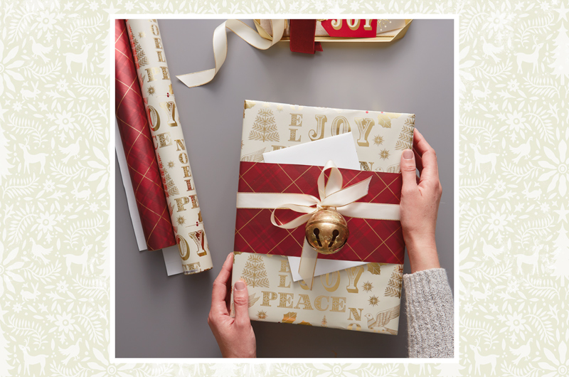 A wrapped Christmas gift accented with a band of coordinating wrap, a satin ribbon and a gold jingle bell.