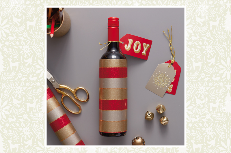 A bottle of wine wrapped with gift wrap and accented with a gift tag that reads, 