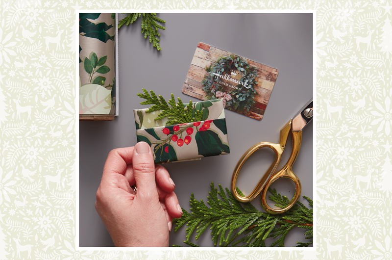 A gift card wrapped with gift wrap and accented with a small sprig of greenery.