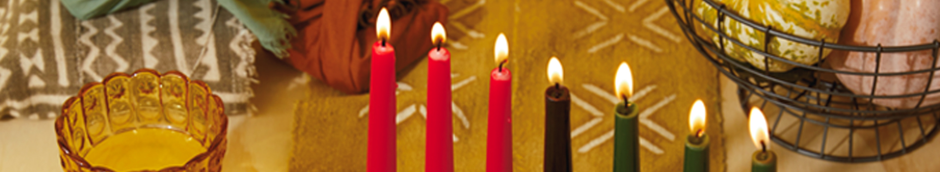 A Kwanzaa Kinara filled with lit candles on a table full of winter squash and celebratory food.