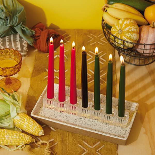 A Kwanzaa Kinara filled with lit candles on a table full of winter squash and celebratory food.