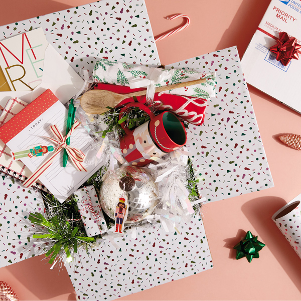 A Christmas care package containing a note pad, address book, tea towel set, nutcracker mug and candle.