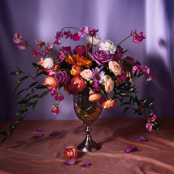A bouquet of flowers in a metallic vase in a moodily lit environment.