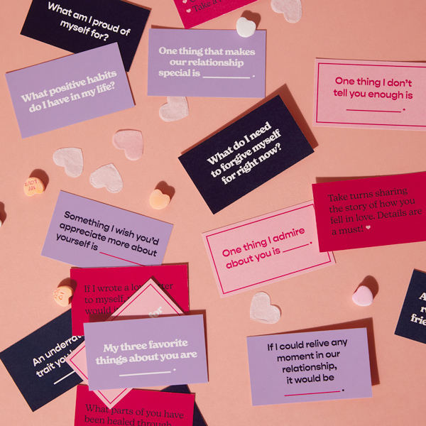 Conversation cards scattered across a table top strewn with candy conversation hearts and tissue paper heart confetti.