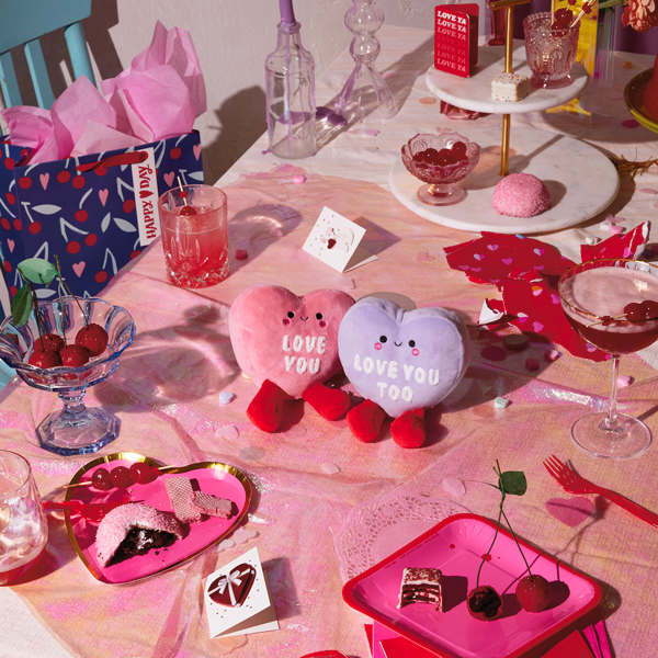 A pair of conversation heart magnetic plushes sits at the center of a table decorated for a Valentine's Day cocktail party.