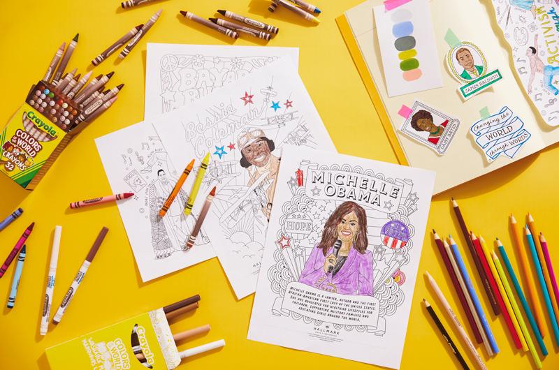 A scrapbook lays on a bright yellow surface. Scattered around the work surface are Black History Month coloring pages, as well as various coloring tools.