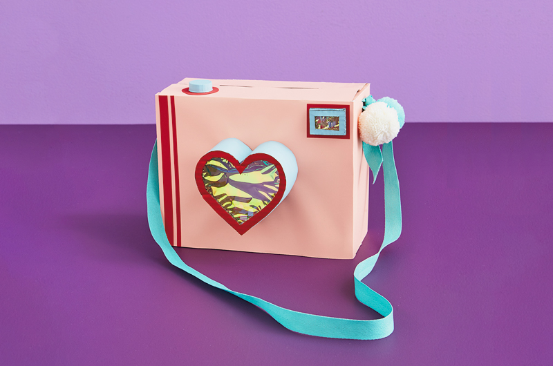 A valentine box shaped like a camera with a strap and a heart shaped lens.