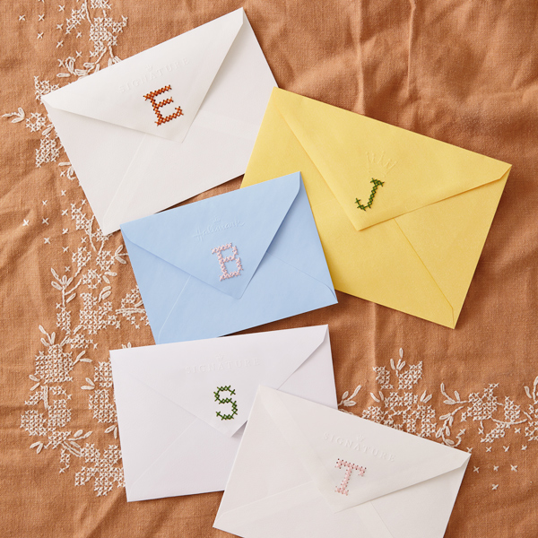 Five card envelopes, each with a different monogram initial cross-stitched on the back flap.