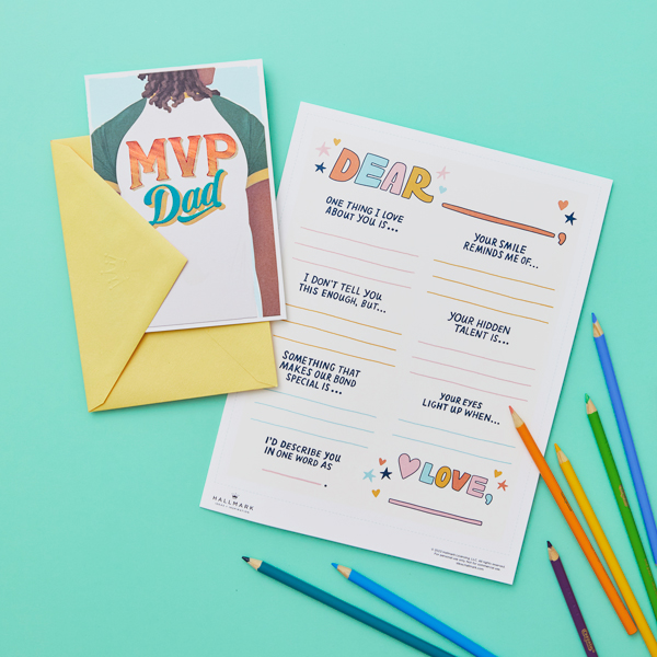 Our free printable writing prompts page for Father's Day on an aqua colored surface with a Father's Day card and colored pencils.