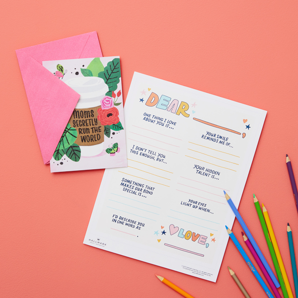 Our free printable writing prompts for Mother's Day page on a coral surface next to a Mother's Day card and colored pencils.