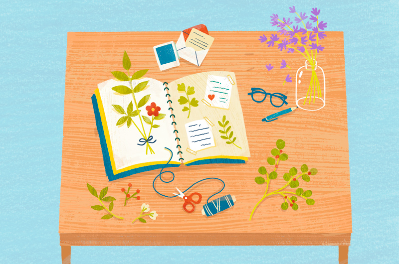 An illustration of a scrapbook lying on a desktop, surrounded by florals for pressing and photos to be pasted into the book.