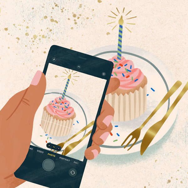 An illustration of a hand holding an iPhone as it captures a cupcake with a lit candle and sprinkles sitting on a plate with a gold fork and knife.