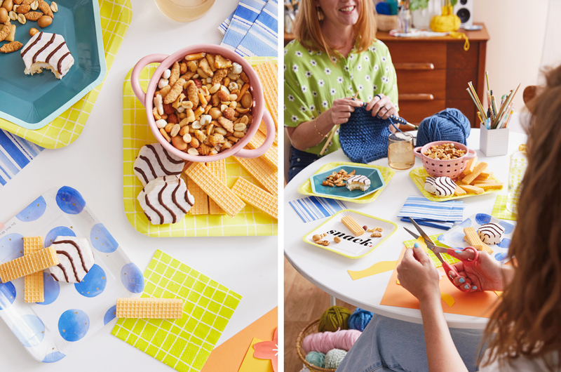 A downshot of a bright, colorful craft party table set with Celebrate! partyware in shades of blue and bright yellow; next to this is a scene from the craft party, in which a smiling woman knits while talking to her friend across the table who is doing cut paper art.