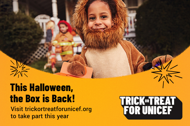 A child in a lion costume holds a Trick-or-Treat for UNICEF collection box.