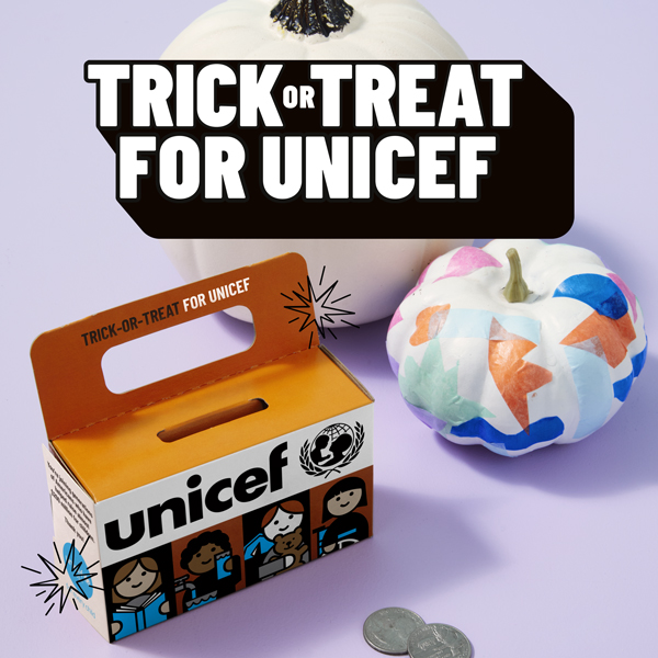 A Trick-or-Treat for UNICEF collection box sits on a light purple surface next to a pair of painted and decoupaged pumpkins; above the grouping is the Trick-or-Treat for UNICEF logo.